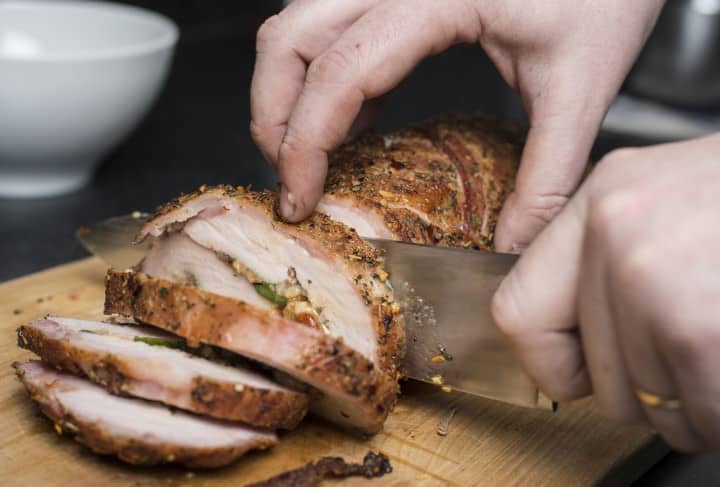 Slicing filled pork fillet on wooden board