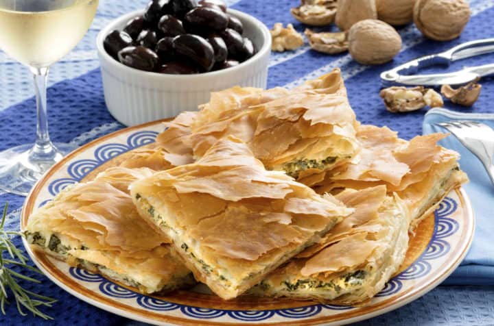 Spanakopita, Greek spinach pie with feta cheese and filo party on on plate with Greek white wine, olives and walnuts