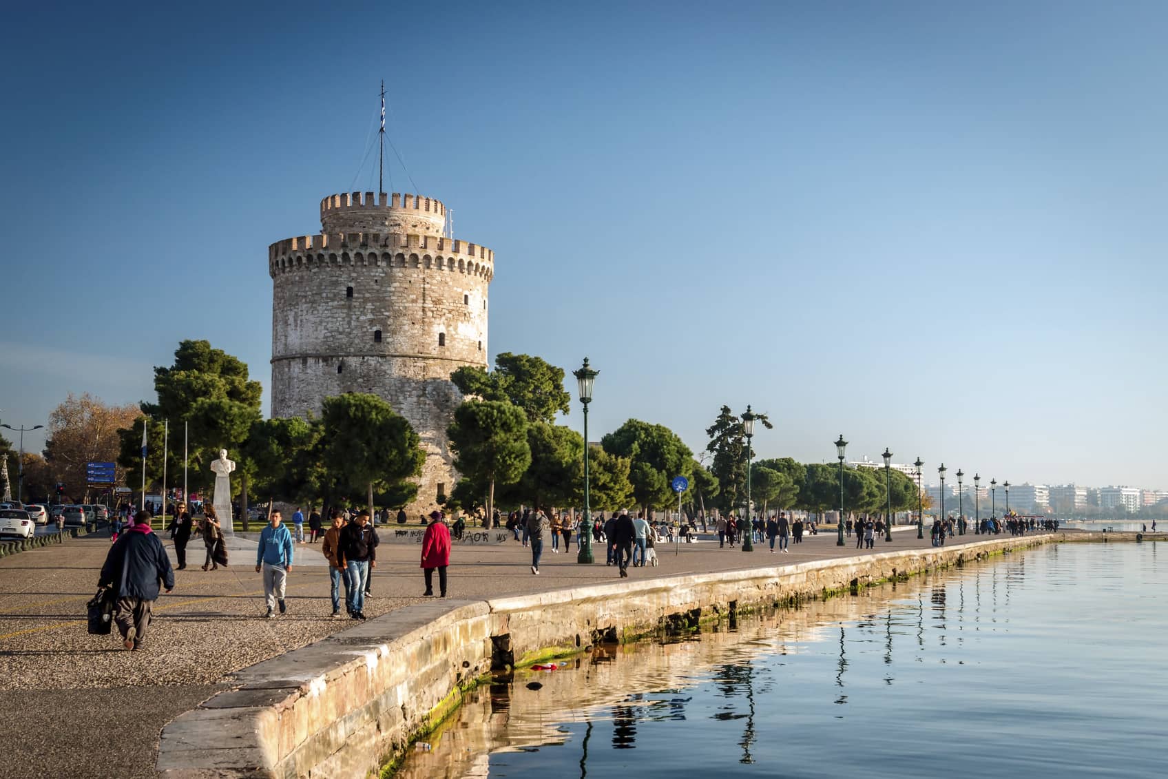 Thessaloniki, Greece - December 24, 2015: People walking on the coast in Thessaloniki next to the white tower which once guarded the eastern end of the city's sea walls